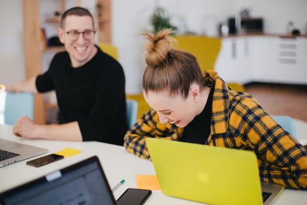 Büro team lacht zusammen ein Mann schwarzes Tshirt mit Frau gelbe karierte Weste